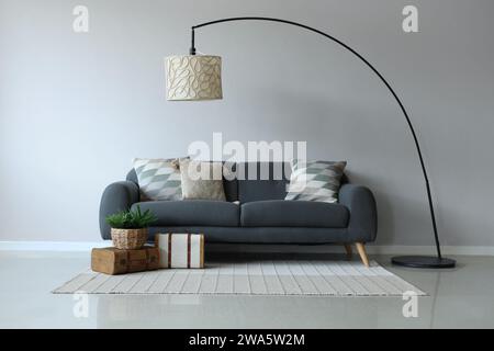 Graues Sofa mit weichen Kissen in der Nähe der weißen Wand Stockfoto