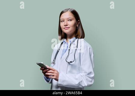 Junge Ärztin mit Smartphone, auf grünem Atelierhintergrund Stockfoto