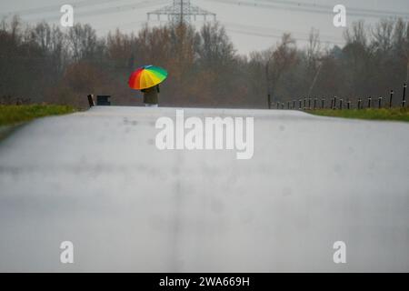 Bad Vilbel, Deutschland. Januar 2024. Eine Frau geht bei regnerischem Wetter auf dem Radweg entlang der Nidda spazieren. Die Nidda-Höhe ist derzeit nicht kritisch, wird aber aufgrund der starken Regenfälle voraussichtlich steigen. Darlegung: Andreas Arnold/dpa/Alamy Live News Stockfoto