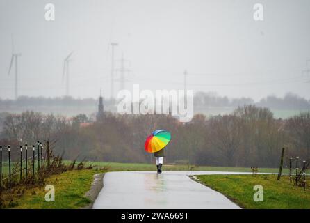 Bad Vilbel, Deutschland. Januar 2024. Eine Frau geht bei regnerischem Wetter auf dem Radweg entlang der Nidda spazieren. Die Nidda-Höhe ist derzeit nicht kritisch, wird aber aufgrund der starken Regenfälle voraussichtlich steigen. Darlegung: Andreas Arnold/dpa/Alamy Live News Stockfoto