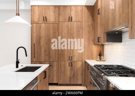 Ein Küchendetail mit Holzschränken, schwarzem Wasserhahn, Bronzelicht, die über der weißen Marmorarbeitsfläche hängt, und einem weißen U-Bahn-Backsplash. Stockfoto