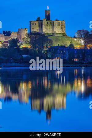 Blick in der Abenddämmerung auf Warkworth Castle und Warkworth Village, die sich im Fluss Coquet spiegeln, wie man von einem Spaziergang mit Warkworth Castle im Flutlicht sehen kann. Stockfoto