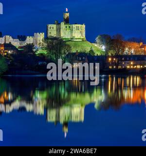Blick in der Abenddämmerung auf Warkworth Castle und Warkworth Village, die sich im Fluss Coquet spiegeln, wie man von einem Spaziergang mit Warkworth Castle im Flutlicht sehen kann. Stockfoto