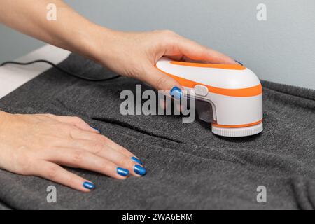 Die Frau entfernt Pillen aus der Kleidung mit einem Pillen-Entferner. Maschine zum Entfernen der Pellets. Die Pillen aus der Kleidung entfernen. Stockfoto