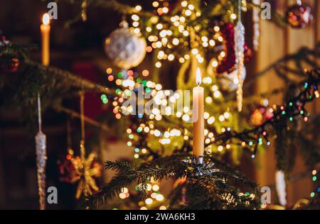 Selektiver Fokus auf Kerzenbrand, Kerzenclip auf echt verziertem Weihnachtsbaum mit Bokeh-Weihnachtslichtern auf Hintergrund. Stockfoto