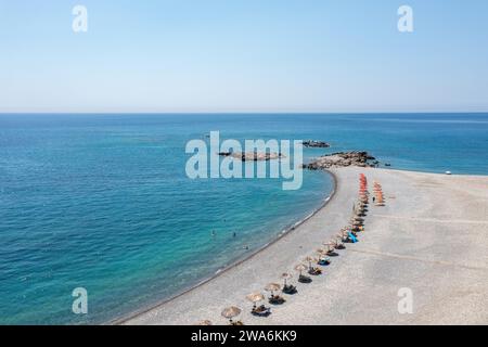 Kieselstrand mit Sonnenschirm in Palaiochora, Kreta, Griechenland. Drohnenblick aus der Luft auf transparentes kristallklares Meerwasser, blauer Himmel, schwimmende Menschen. Stockfoto