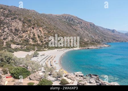 Strand mit Sonnenschirm in Palaiochora Stadt, Kreta, Griechenland. Drohnenansicht aus der Vogelperspektive auf kristallklares Meerwasser der Ägäis, schwimmende Menschen, Felsformationen. Stockfoto