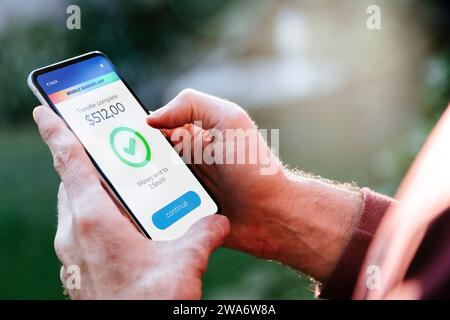 Mann, der online Geld macht, überträgt, indem er Apps verwendet, um Geld zu senden und zu empfangen. Mobiltelefon mit einer Finanzanwendung auf dem Bildschirm. Geldtransfer-Konzept Stockfoto