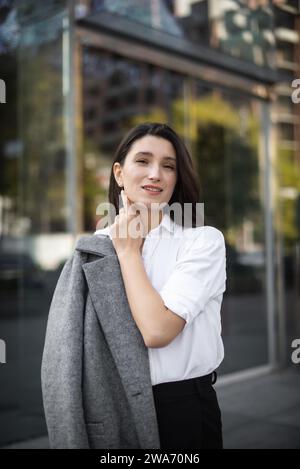 Geschäftsfrau, die in die Kamera blickt, während sie in der Nähe eines modernen Bürogebäudes steht. Stockfoto