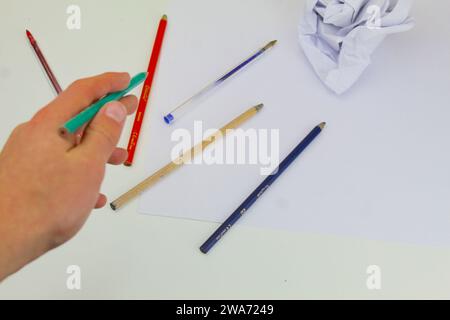 Ein Foto von Malstiften eines Schülers und weißen Papierstücken, die auf einem weißen Schreibtisch zusammengerollt sind. Stockfoto