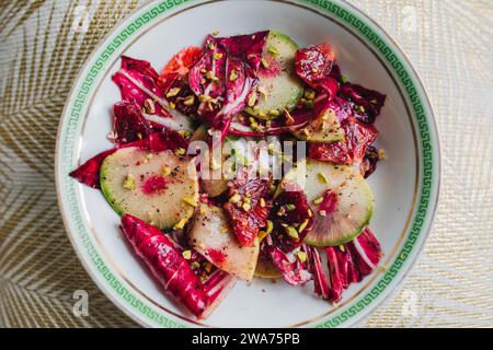 Radicchio Salat mit Wassermelone Rettich, Blutorange, Pistazien auf weißem Teller mit grünem griechischen Schlüssel Stockfoto