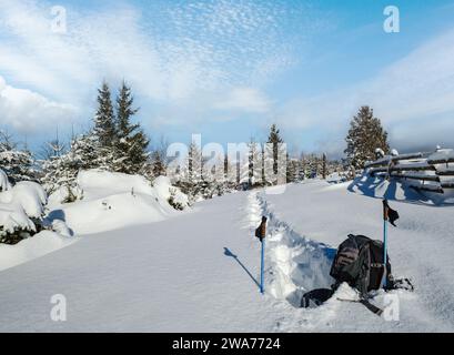 Winter abgelegenen alpinen Dorf Rand, Schneeverwehungen auf Berg Tanne Waldrand. Touristischer Rucksack auf einem frisch ausgetretenen Wanderweg. Stockfoto