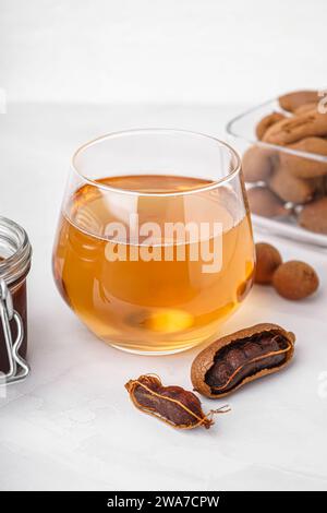 Glas leckeres Tamarindengetränk und Früchte auf weißem Hintergrund Stockfoto