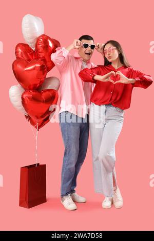 Junges Paar in Sonnenbrille mit Herzballons auf rosa Hintergrund. Valentinstag-Feier Stockfoto