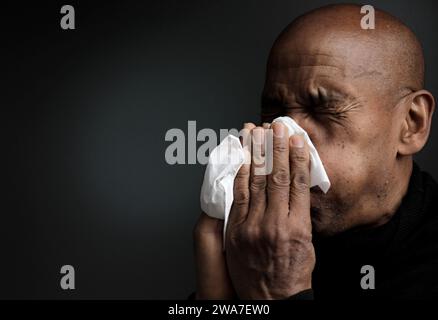 Mann, der die Erkältung und Grippe fängt Mann, der Nase bläst, nachdem er eine Erkältung mit grauem Hintergrund mit Leuten Stock Foto gefangen hat Stockfoto