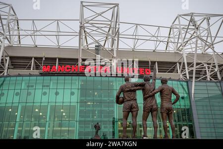 United Trinity Statue mit den Manchester United Legenden George Best, Denis Law und Sir Bobby Charlton auf dem Bild mit Blick auf das Old Trafford Stadion und die S Stockfoto