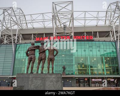 United Trinity Statue mit den Manchester United Legenden George Best, Denis Law und Sir Bobby Charlton auf dem Bild mit Blick auf das Old Trafford Stadion und die S Stockfoto