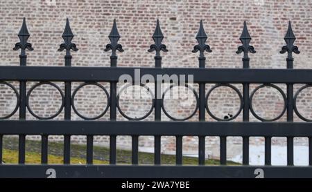 Schöner schwarzer dekorativer Gusseisenzaun mit künstlerischer Schmiedekunst. Einzäunung frontalnah in einem sich wiederholenden Muster vor einer gemauerten Mauer Stockfoto