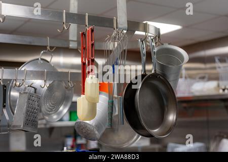 Töpfe und Pfannen aus Edelstahl und andere Kochutensilien hängen in einer gewerblichen Industrieküche. Stockfoto