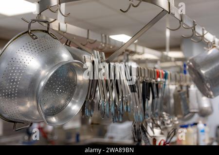 Töpfe und Pfannen aus Edelstahl und andere Kochutensilien hängen in einer gewerblichen Industrieküche. Stockfoto