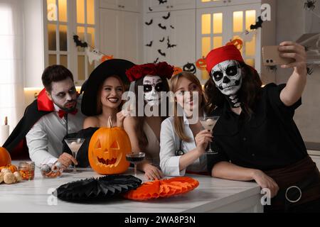 Gruppe von Leuten in gruseligen Kostümen mit Cocktails, die auf der Halloween-Party drinnen Selfie machen Stockfoto