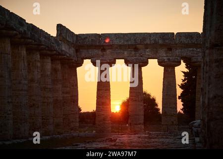 Die Sonne untergeht malerisch zwischen den alten Säulen einer Ruine, Sommerabendstimmung in Paestum, einer antiken Stadt 35 Kilometer südlich von Salerno. Gefunden Stockfoto