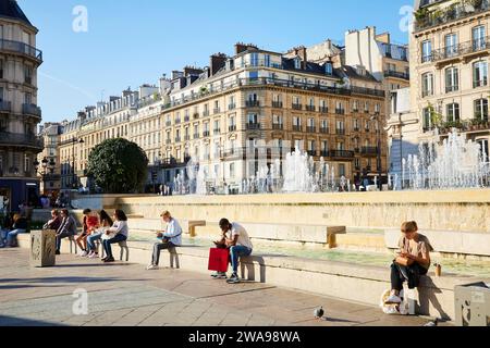 Menschen sitzen am Brunnen in der Sonne auf der Rue de Rivoli vor dem Rathaus Paris im Parvis de l'Hotel de Ville Stockfoto