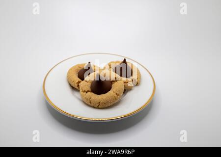 Aus nächster Nähe sehen Sie drei hausgemachte Erdnussbutter-Kekse mit einem Schokoladentropfen auf einer weißen Porzellanplatte Stockfoto