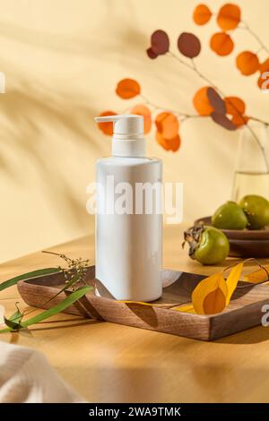 Eine Pumpflasche ohne Etikett auf einem Holztablett mit gelben und grünen Blättern. Weiße Flasche für Gesichtscreme, Reinigungsmittel, Körperlotion oder Shampoo Stockfoto