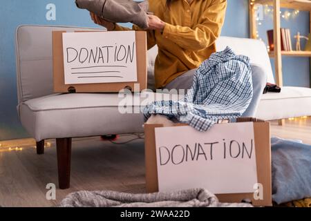 Konzept des Wohltätigkeits- und Bekleidungsrecyclings. Eine junge Frau steckt bunte Kleidung in eine Spendenbox. Stockfoto