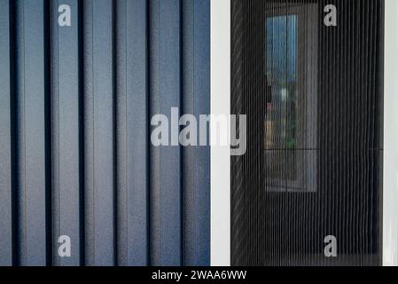 Haus mit einer Fassade bedeckt mit dunkelblauen PVC-Paneelen und Fliegengitter an den Fenstern Stockfoto