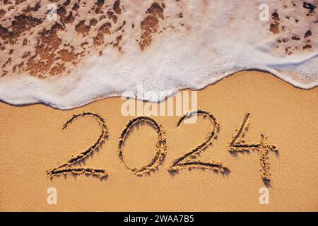Neujahrstext 2024 geschrieben am Strand Sand und Welle bei Sonnenaufgang Stockfoto