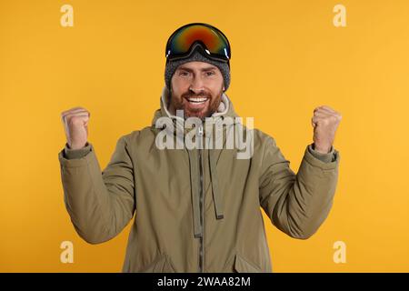 Wintersport. Fröhlicher Mann in Skianzug und Brille auf orangem Hintergrund Stockfoto