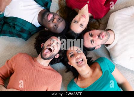 Eine bunte Gruppe von Freunden, die sich hinlegen und lustige Selfies im Kreis machen, das Gesicht ziehen Stockfoto