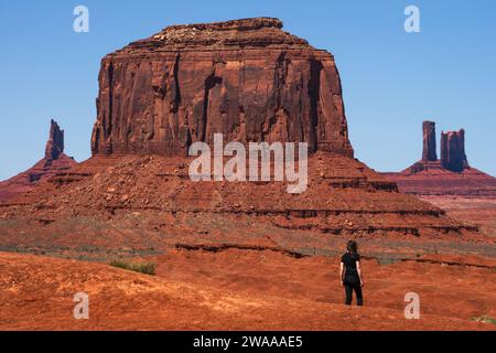 Eine schwarz gekleidete Frau, die die Felsformation im Monument Valley, Utah, USA, bewundert. Blauer Himmel und helles Tageslicht. Fäustlinge, Orange Rocks, Frühlingszeit. Stockfoto