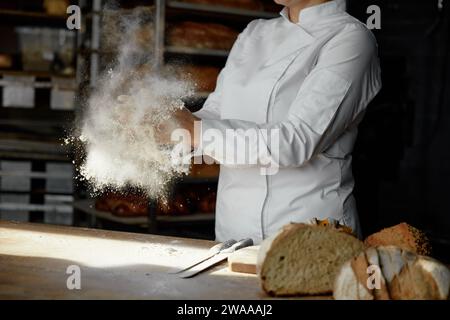 Nahaufnahme weibliche Köcherhände klatschen in einer Wolke aus pulverförmigem Mehl über dem Tisch Stockfoto