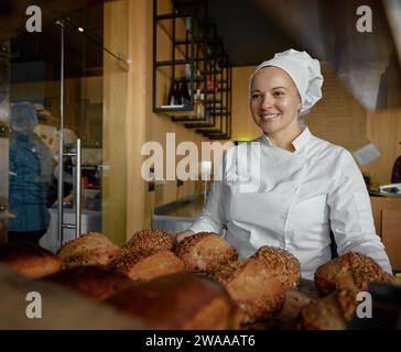 Porträt einer fröhlichen Bäckerin, die leckeres frisches Brot anbietet Stockfoto