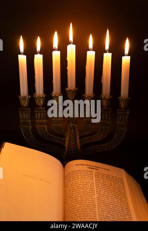 Die Heilige Bibel ist offen für das Buch Genesis in Kapitel 1 und Menora mit 7 Kerzen isoliert auf dunklem Hintergrund. Stockfoto