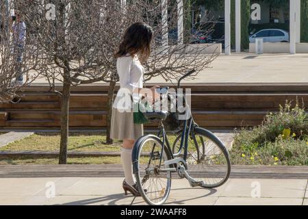 Eine schöne junge Frau steht an einem sonnigen Wintertag mit dem Fahrrad auf dem Stadtplatz. Stockfoto