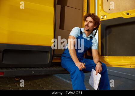 Ein junger Kurier im Overall sitzt im Minivan Stockfoto