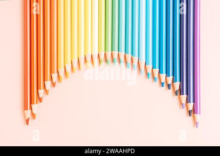 Farbige Regenbogenstifte liegen in einer Reihe auf beigefarbenem Hintergrund Stockfoto