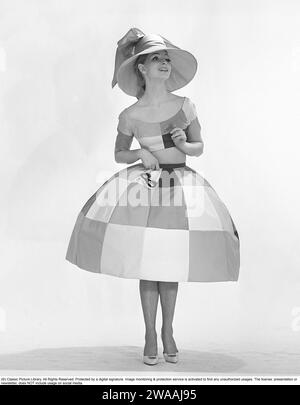 In den 1960er Jahren Ein Modemodell in einem Studio, das ein außergewöhnliches Designerkleid aus einem Stoff mit großen Quadraten in verschiedenen Farben und einem ebenso auffälligen breiten Hut trägt. 1962 Kristoffersson Ref. CY35-12 Stockfoto