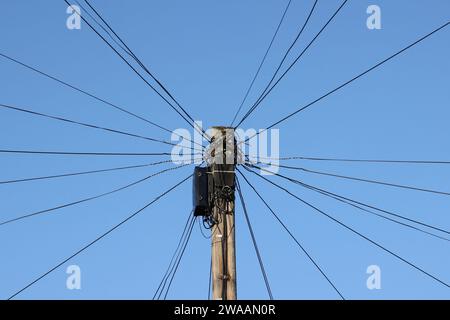 Telegrafenmast mit vielen Drähten und einer Abzweigdose gegen einen blauen Himmel Stockfoto