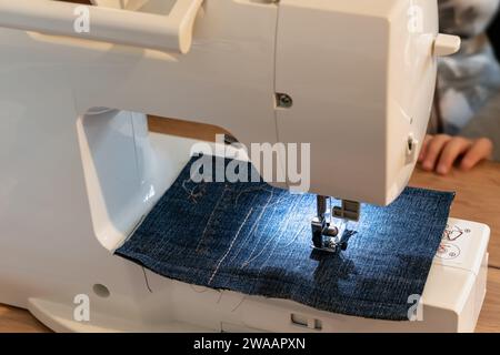 Mann, der eine Nähmaschine mit blauem Kleidungsstück benutzt, für Reparaturarbeiten, Personalisierung, Kreation, Upcycling Stockfoto