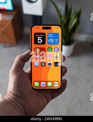 LONDON – 05. NOVEMBER 2023: Apple iPhone 14 Pro wird in der Hand gehalten mit einem leuchtend orangefarbenen Hintergrundbild auf dem Bildschirm Stockfoto