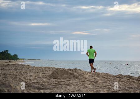 Rückansicht eines Mannes, der am Morgen am Strand entlang joggt, männliche Athleten, die entlang der Küste laufen Stockfoto