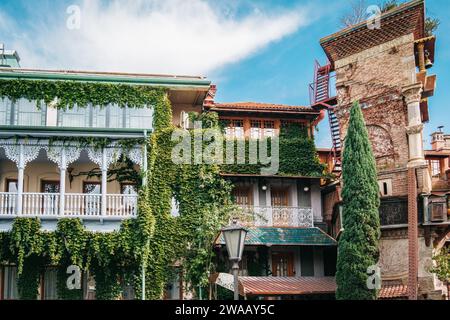 Wunderschönes traditionelles georgianisches Haus mit Weinstöcken auf dem Holzbalkon neben dem Schiefen Uhrenturm in der Altstadt von Tiflis, Georgien Stockfoto