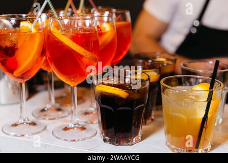 Eine einladende Auswahl an farbenfrohen Cocktails, darunter Aperol Spritz und Cuba Libre, geschmückt mit Zitrusscheiben, die auf einem gesellschaftlichen Event genossen werden können Stockfoto