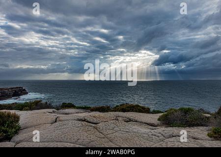 Sonnenstrahlen, die durch ein Loch in den Wolken über dem Meer leuchten, kurz nach Sonnenaufgang, zwischen Maroubra Beach und Malabar Beach, Randwick, Sydney, Australien. Stockfoto