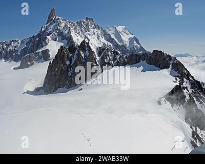 Blick auf die schneebedeckten Berge in der Region Monte Bianco (Mont Blanc) der italienischen Alpen mit winzigen Ameisenklettern auf dem Weg durch das Schneefeld Stockfoto